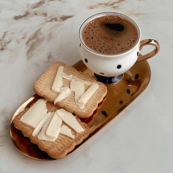 A cup of coffee on a gold tray with buttered biscuits, set against a marble surface.
