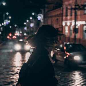 Silhouette of a woman walking on a bustling city street at night with blurred car lights.