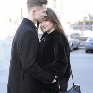A loving couple in black coats embraces on a sunny day in Kyiv, Ukraine.