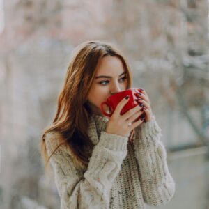 Young woman sipping coffee in a cozy sweater outdoors, conveying warmth and relaxation.